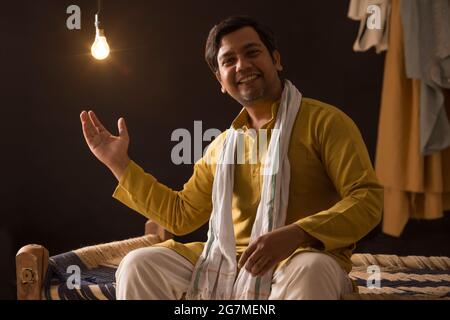 EIN FRÖHLICHER DORFBEWOHNER MIT ERHOBENER HAND, DER VOR DER KAMERA POSIERT Stockfoto