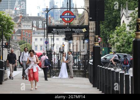 London, England, Großbritannien. Juli 2021. Ein ostasiatisches Paar posiert für ihre Hochzeitsfotografen vor der Westminster Station in London, während Menschen vorbeikommen. In Großbritannien gibt Â es ab dem 19. Juli keine Grenzen für die Anzahl der Personen, die an Gottesdiensten oder Empfängen teilnehmen können, unabhängig vom Veranstaltungsort. Die aktuellen Regeln für soziale Distanzierung und Gesichtsbedeckung gelten nicht mehr, es gibt keine Anforderungen für Tischservice, Und Einschränkungen beim Singen und Tanzen werden ebenfalls enden. Quelle: Tayfun Salci/ZUMA Wire/Alamy Live News Stockfoto