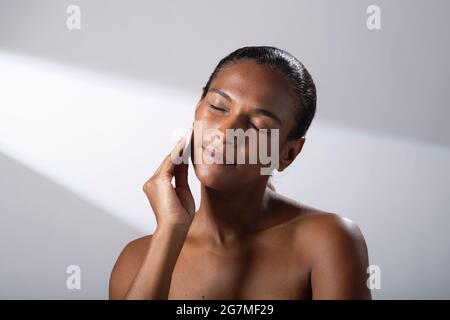 Schönheitsbilder einer Frau mit dunklerem Hautton. Kopf- und Schulterbilder einer zufriedenen, glücklichen Dame mit Baumwoll-Gesichtspads. Stockfoto