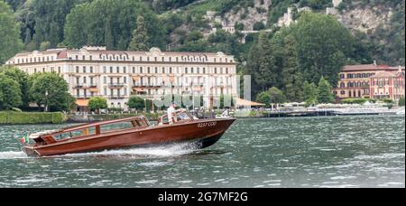 COMO, ITALIEN - 12. JULI: Schnelles Motorboot segelt Seewasser mit grüner Küste im Hintergrund, aufgenommen am 12. juli 2021 im Sommer in der Nähe von Cernobbio, Como, IT Stockfoto