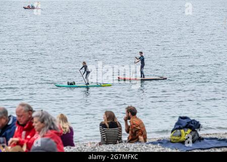 Urlauber auf Stand Up Paddleboards paddeln an einem kalten Tag in Cornwall am Strand von Polgwidden Cove am Helford River vorbei. Stockfoto