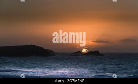 Ein Panoramablick auf einen intensiven spektakulären Sonnenuntergang über der Fistral Bay in Newquay in Cornwall. Stockfoto