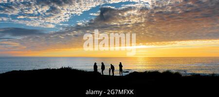 Panoramabild von Urlaubern, die von einem wunderschönen, farbenfrohen Sonnenuntergang über Little Fistral an der Küste von Newquay in Cornwall umraunt werden. Stockfoto