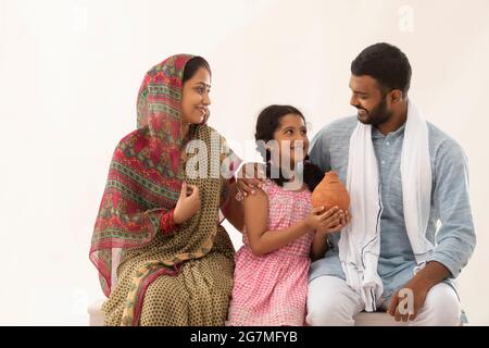 PORTRÄT EINER LÄNDLICHEN ELTERN MIT TOCHTER, DIE EINE SCHLAMMSCHWEINBANK HÄLT Stockfoto