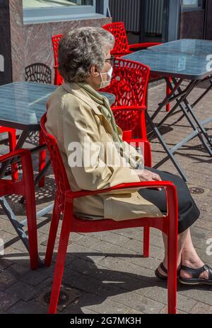 Ältere Frau mit Gesichtsmaske auf Café-Stuhl sitzend - Brüssel, Belgien. Stockfoto