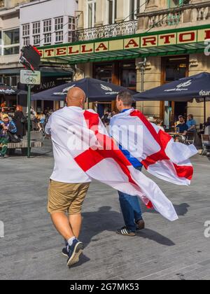 Zwei britische Fußballfans der Euro 2021, die mit der Flagge von St. George über den Schultern durch die Brüsseler Innenstadt laufen Stockfoto