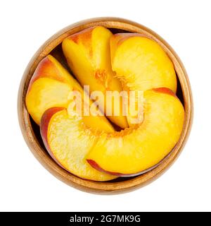 Pfirsich in einer Holzschüssel schneiden. Geschnittene reife Früchte, mit einem gelben und saftigen Fruchtfleisch und samtiger Haut. Prunus persica. Bereit zum Essen. Stockfoto