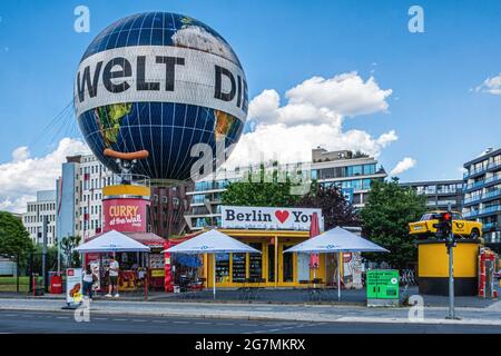 Fastfood-Stall mit Wurstwaren, Ballonfahrt mit Festungsballon und gelbes Trabi-Auto. Sehenswürdigkeiten in Mitte, Berlin, Deutschland. Stockfoto