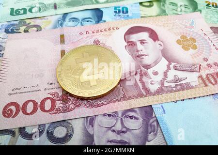 Nahaufnahme einer goldenen Zcash-Münze auf einem Stapel thailändischer Baht-Banknoten. Stockfoto