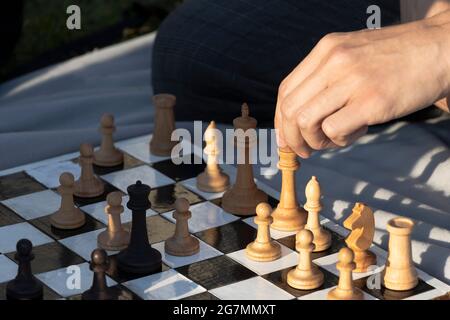 Junger Mann, der eine Bewegung durch Holzschach macht. Schach spielen im Park. Selektiver Fokus. Stockfoto