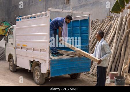 ZWEI ARBEITER ENTLADEN ZUSAMMEN EINEN LASTWAGEN MIT HOLZMASTEN Stockfoto