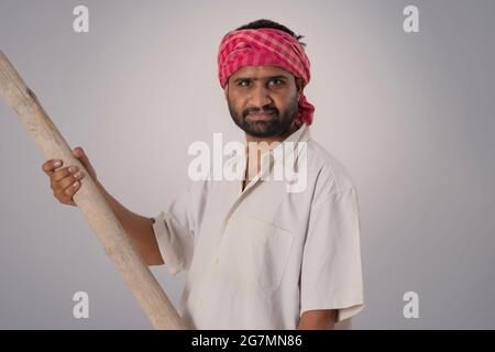 PORTRÄT EINES ARBEITERS, DER EINEN STOCK HÄLT UND DIE KAMERA ANSCHAUT Stockfoto