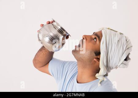 EIN ARBEITER, DER WASSER AUS EINEM STAHLTOPF TRINKT Stockfoto