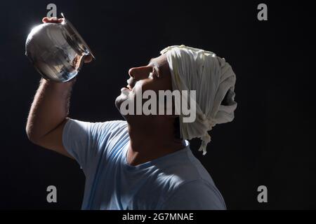 EIN ARBEITER, DER NACHTS WASSER AUS EINEM STAHLTOPF TRINKT Stockfoto