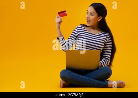 Eine junge Frau mit Laptop schaut sich ihre Kreditkarte online an. Stockfoto