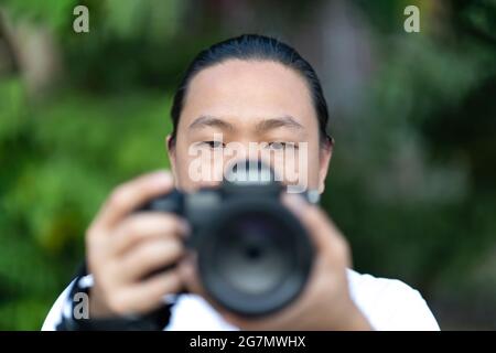 Konzentrieren Sie sich auf das asiatische Männergesicht, das er die Blur Medium Format Camera in der Hand hält, und bereiten Sie sich auf die Aufnahme vor ihm vor. Stockfoto