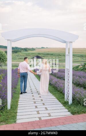 Zurück in voller Länge Ansicht von glücklich liebenswürdig mittleren Alters Paar, zu Fuß auf dem Weg in Lavendel Feld, Hände halten und eine tolle Zeit zusammen Stockfoto