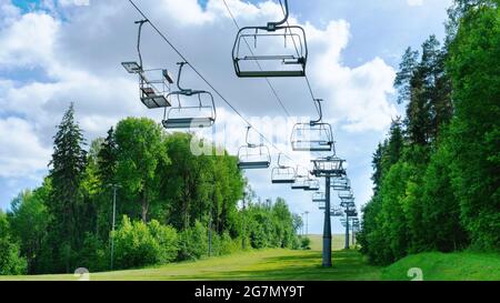 Skilift im Sommer gegen den blauen Himmel. In der Nebensaison ist der Skikomplex menschenleer. Der Sessellift mit leeren Kabinen funktioniert nicht auf sonniger Basis Stockfoto