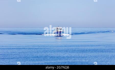 Motorboot, das auf dem Hintergrund der gekräuselten Ägäis navigiert, Pfad auf ruhigem Wasser. Griechenland, Kykladen. Ruhige Wasseroberfläche, klarer Himmel. Sommerferien concep Stockfoto