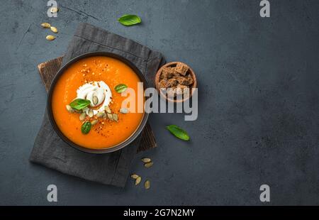 Kürbissuppe mit Rahm und Karotten auf dunkelgrauem Hintergrund. Draufsicht, Kopierbereich. Stockfoto