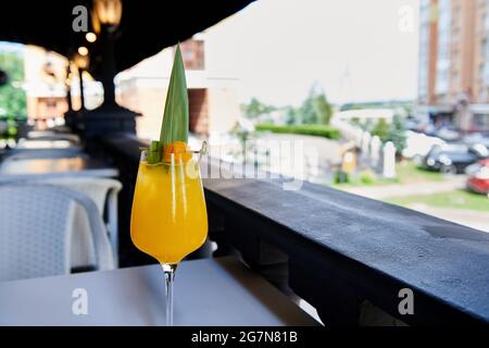 Gelbe Mango-Limonade, verziert mit Mangoscheibe und Bambusblatt. Alkoholcocktail mit Eis im leeren Restaurant. Erfrischendes Getränk in nassem Glas. Stockfoto