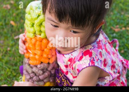 Close up kleine asiatische Kind hält bunte Fischfutter, entzückende Mädchen in hübschen Kleid am Sommertag im Park . Im Freien Stockfoto