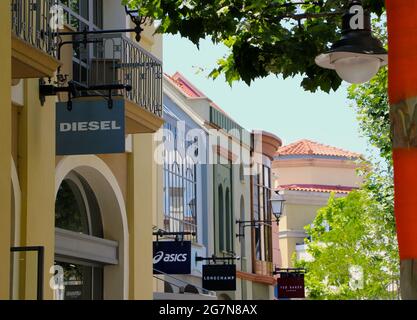 Las Rozas Outlets Einkaufszentrum mit Schildern für Diesel, Asics und Longchamp mit orangefarbenen Streifen auf Baumstämmen an einem sonnigen Sommernachmittag Madrid Spanien Stockfoto