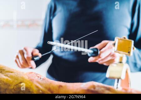 Anonyme Person schärft Schinkenmesser vor dem Schneiden von Schinken. Sehr gut geschärftes Qualitätsmesser. Mittelteil des scharfen Messers des männlichen Küchenchefs. Stockfoto