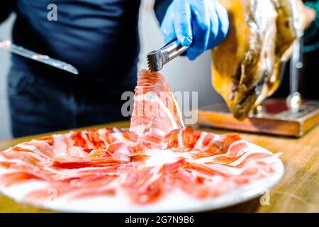 Schinkenplatte. Appetitlich traditionelle spanische köstliche Scheibe iberische jamón oder Schinken-Bein geheilt. Person, die eine Pinzette hält. Spanisches Gourmetessen. Typisch Spani Stockfoto