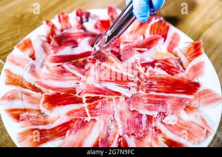Schinkenplatte. Appetitlich traditionelle spanische köstliche Scheibe iberische jamón oder Schinken-Bein geheilt. Person, die eine Pinzette hält. Spanisches Gourmetessen. Typisch Spani Stockfoto