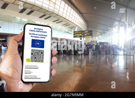 Französisches EU Digital COVID Zertifikat mit dem QR-Code auf dem Bildschirm eines Mobiltelefons, das von einer Hand gehalten wird, mit verschwommenem Flughafen im Hintergrund. Übersetzung aus Stockfoto