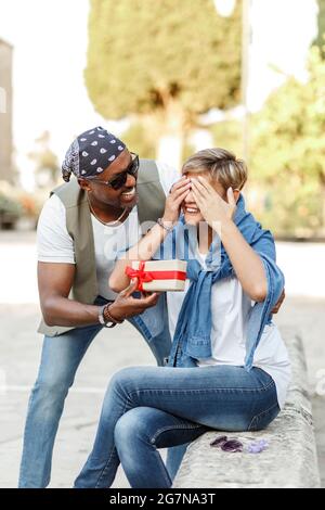 Glücklich mittleren Alters interracial paar sitzen. Mann, der seiner Frau, Freundin oder Frau ein Geschenk zum Valentinstag gibt. Stockfoto