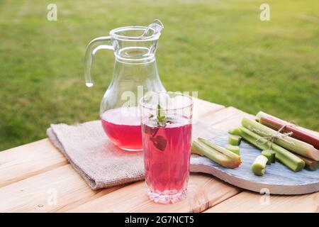 Trinken Sie von den Rhabarberstielen auf dem hölzernen Tisch im Freien. Stockfoto