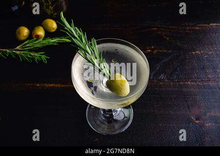 Smoked Rosmarin Oil Dirty Martini: Ein Dirty Gin martini, der in einem Coupé-Glas serviert und mit einem Rosmarinzweig in einer grünen Olive garniert wird Stockfoto