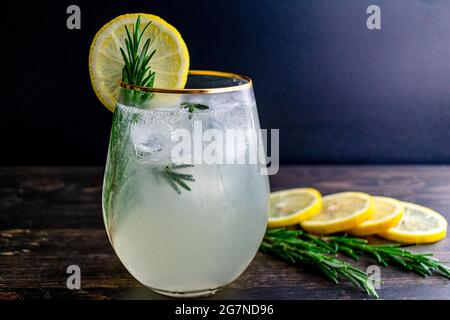 Rosemary Gin Fizz Cocktail mit Garnierung: Ein Gin, Zitrone und Rosmarin-Cocktail, der über Eis serviert und mit einer Zitronenscheibe und einem Rosmarin-Zweig garniert wird Stockfoto