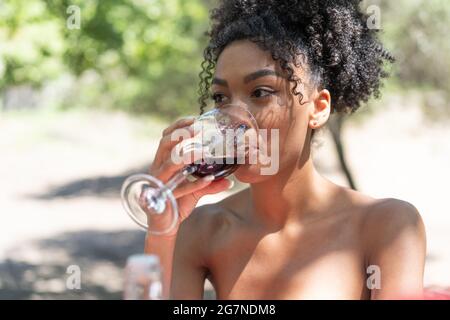 Junge Frau afrikanischer Abstammung, die auf dem Land Rotwein trinkt Stockfoto