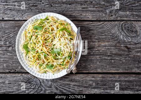 Sommer-Spaghetti alla carrettiera mit Minzblättern, Zitronenschale, Pecorino-Käse, Chilischoten-Flocken, Petersilie und geriebenen Zucchini auf einem weißen Teller Stockfoto