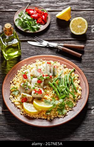 Bacalhau com todos, Kabeljau mit Bulgur, gedämpfte grüne Bohnen, bestreut mit scharfer Chilischote und Frühlingszwiebeln auf einem rustikalen Teller, auf einem Holztisch, por Stockfoto