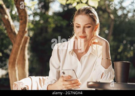 Erfolgreiche junge Geschäftsfrau, die im Café im Freien sitzt und das Smartphone benutzt Stockfoto