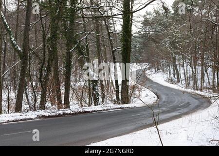 Im Winter schlängelt sich eine Straße durch ein schneebedecktes Waldgebiet. Stockfoto