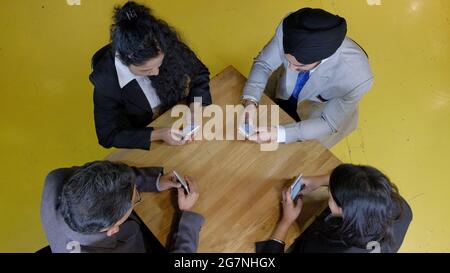Eine Gruppe von Indern, die mit ihren Smartphones im Büro um den Tisch sitzen Stockfoto