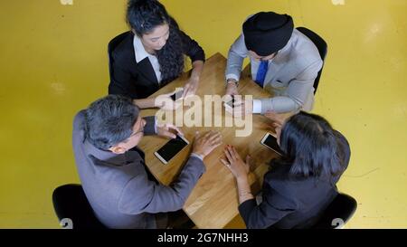 Eine Gruppe von Indern, die mit ihren Smartphones im Büro um den Tisch sitzen Stockfoto