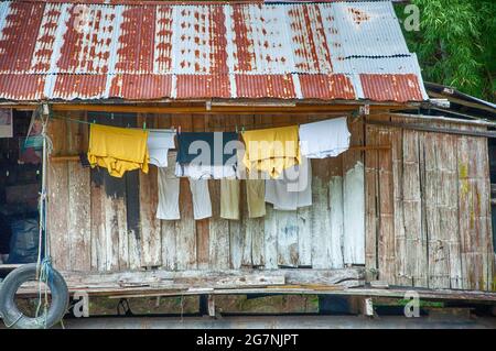 Kleidung, die auf einer rustikalen, schwimmenden Hütte auf dem Wasser in Thailand hängt. Stockfoto