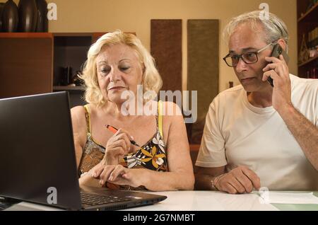 Reife Männer und Frauen zu Hause, die aufgrund der Zusammenarbeit mit einem Laptop und einem Mobiltelefon Geschäfte über das Internet führen Stockfoto