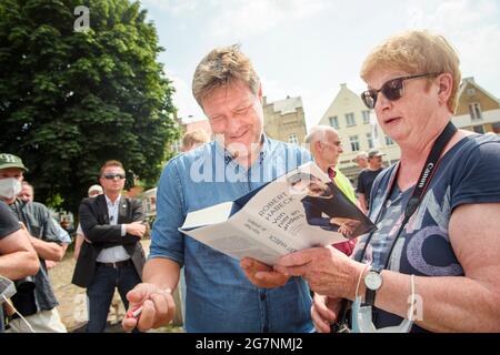 Friedrichstadt, Deutschland. Juli 2021. Robert Habeck, Co-Vorsitzender von Bündnis 90/die Grünen, signiert sein Buch ('von hier an anders') vor dem Beginn einer Wahlkampfveranstaltung im Rahmen seiner 'Küstenreise' durch Schleswig-Holstein vor einem Bürger auf dem Marktplatz in Friedrichstadt. Quelle: Gregor Fischer/dpa/Alamy Live News Stockfoto