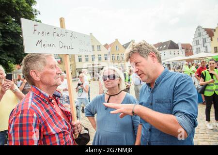 Friedrichstadt, Deutschland. Juli 2021. Robert Habeck (r), Mitvorsitzender von Bündnis 90/die Grünen, Und Christine Axe (m), Vorsitzende der Grünen in Friedrichstadt, spricht vor dem Beginn einer Wahlkampfveranstaltung im Rahmen der Habeck-Küstentour durch Schleswig-Holstein mit einer Bürgerin, die ein Schild ("Free ride for my Diesel") auf dem Marktplatz in Friedrichstadt hält. Quelle: Gregor Fischer/dpa/Alamy Live News Stockfoto