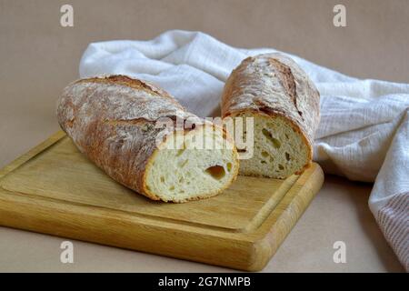 Brotlaib, in zwei Stücke geschnitten, auf Holzschneidebrett. Gebackenes Brot und Geschirrtuch auf Bastelpapier, selbstgebackenes Brot. Bio gesunde Ernährung. Stockfoto