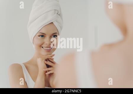 Gesunde junge Frau mit sauberer Haut lächelt beim Auftragen von Gesichtscreme Stockfoto