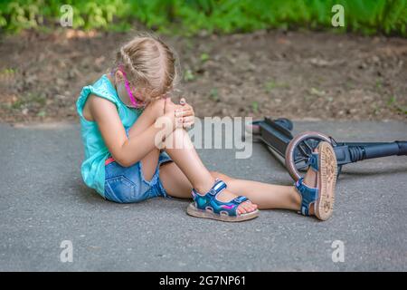 Trauma auf dem Roller. Ein fünfjähriges Mädchen fiel in einem Park auf einen Roller und verletzte sich schwer ihr Knie. Elektroroller Verletzung Konzept. Stockfoto