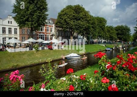 Friedrichstadt, Deutschland. Juli 2021. Zwei Stand-up-Paddler reiten bei sonnigem Wetter in einem Kanal in Friedrichstadt an einem Café vorbei. Quelle: Gregor Fischer/dpa/Alamy Live News Stockfoto